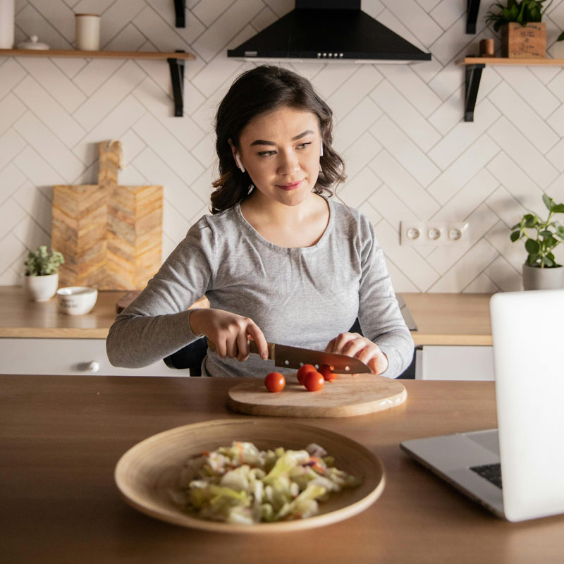 person cutting tomatoes while looking at computer